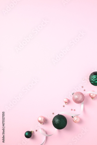 Pink and green Christmas baubles with ribbon on pastel pink background.