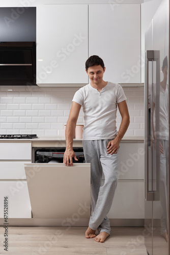 handsome husband man using dishwasher and washing dishes in white modern kitchen