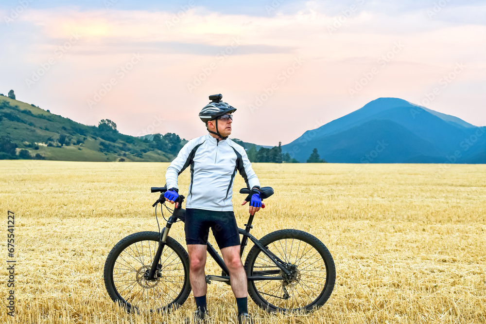 Fototapeta premium the cyclist with the bike resting on straw harvested field