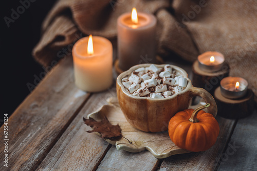 Spicy sweet fall hot drink  delicious pumpkin latte with cinnamon  marshmallow with salted caramel. Served in handmade artisan mug in shape of pumpkins  cozy home decor with candles  dry autumn leaves