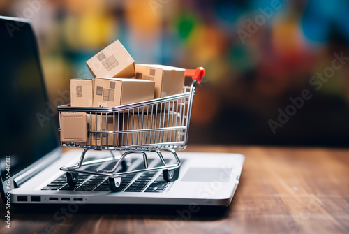 Small shopping cart filled with boxes, standing on a laptop PC. Concept of online shopping on black friday, spring sale, cyber monday. Shallow field of view.