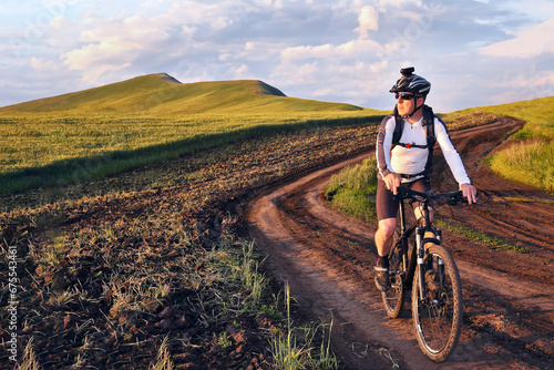 Fototapeta Naklejka Na Ścianę i Meble -  cyclist on bike rides along the fields of wheat in the sunlight