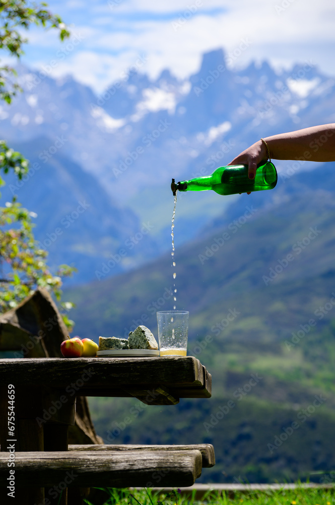 Fototapeta premium Pouring from high height of natural Asturian cider made from fermented apples, Asturian cabrales cow blue cheese with view on Naranjo de Bulnes top of Picos de Europa mountains, Spain