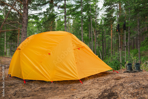 Hiking tourism adventure. Camping picnic orange tent campground in outdoor hiking forest. Touristic boots near camping tent. Campsite in nature at summer trip camp. Trekking travel vacation concept