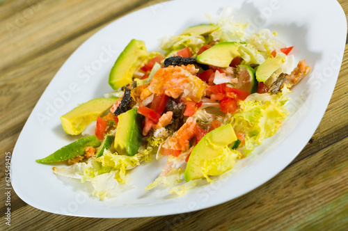 Salad of grilled salmon, fresh avocado, lettuce, tomatoes and lemon served on white platter on wooden background