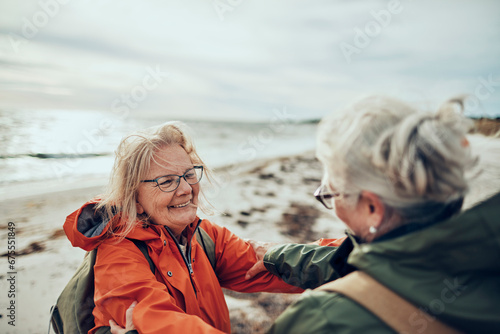 Two senior women laughing together on a chilly beach day photo