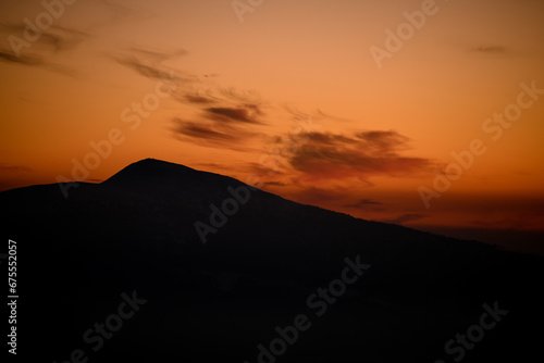 Dark silhouette of mountain with bright orange sunset sky on background