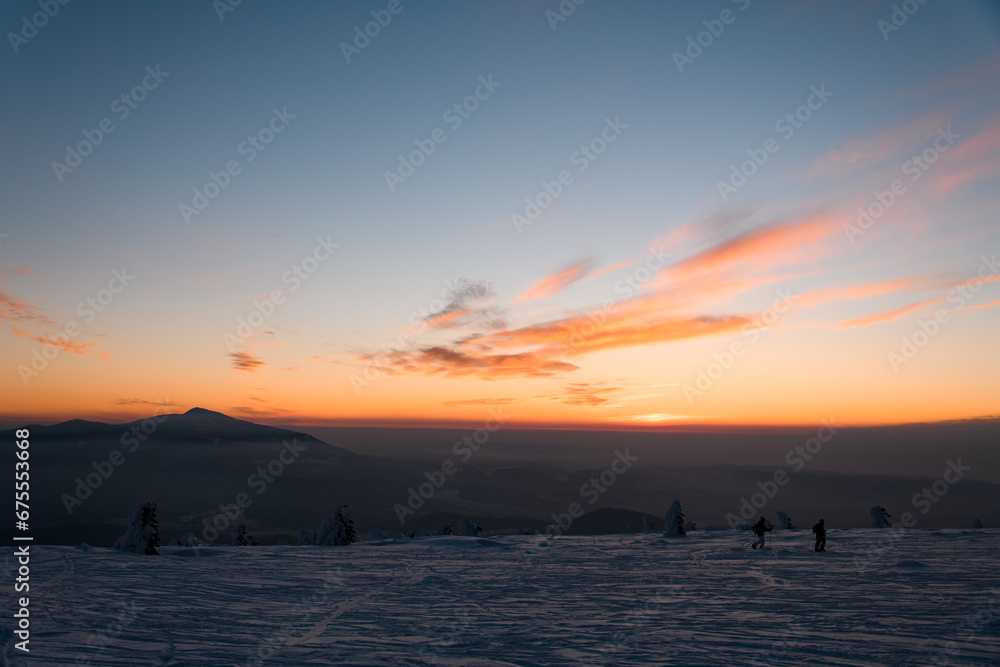 Dynamic silhouettes of skiers walking through the snow against amazing sunset colorful sky.