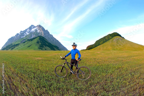 Fototapeta Naklejka Na Ścianę i Meble -  cyclist with a bicycle is resting on a green field against a blue sky. sports and recreation in nature