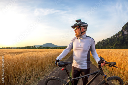 the cyclist with the bike in a field watching the sunset. sports and hobbies. outdoor activities