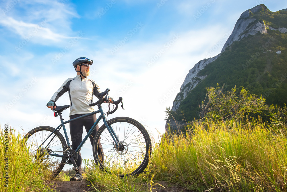 bearded cyclist stands with a bicycle against a background of blue sky and mountains. cycling and health-related hobbies