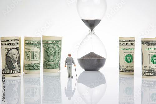 Miniature people. an elderly pensioner man stands near dollar money, an hourglass. concept of time and provision of old age