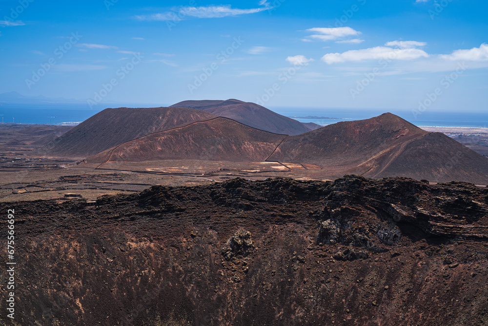 View of a part of the crater of one of the most famous volcanoes on the island and in the background the sea with several more volcanoes. Photography taken in Fuerteventura, Canary Islands, Spain.