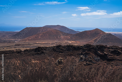 View of a part of the crater of one of the most famous volcanoes on the island and in the background the sea with several more volcanoes. Photography taken in Fuerteventura  Canary Islands  Spain.