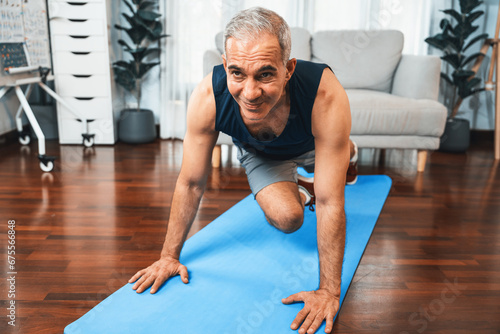 Athletic and active senior man doing exercise on fit mat with plank climbing at home exercise as concept of healthy fit body lifestyle after retirement. Clout