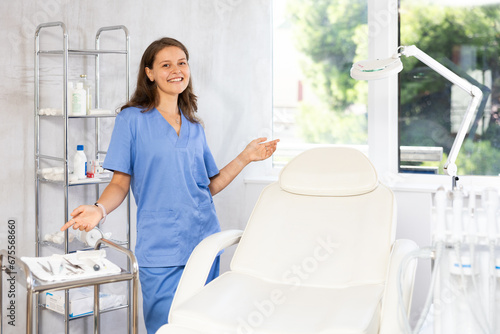 Portrait of positive female doctor cosmetologist wearing overall showing equipment of clinic before procedure