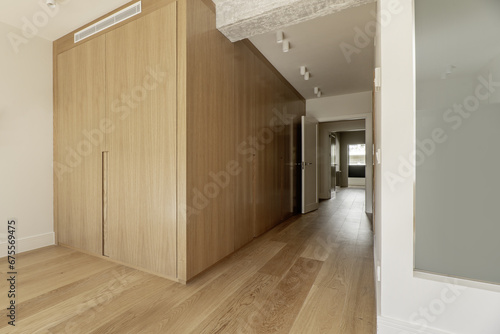 Hallway to a bedroom with built-in wardrobes with custom-made light oak doors, white painted walls, skylight on a bathroom wall, reinforced concrete beams and light wood floors