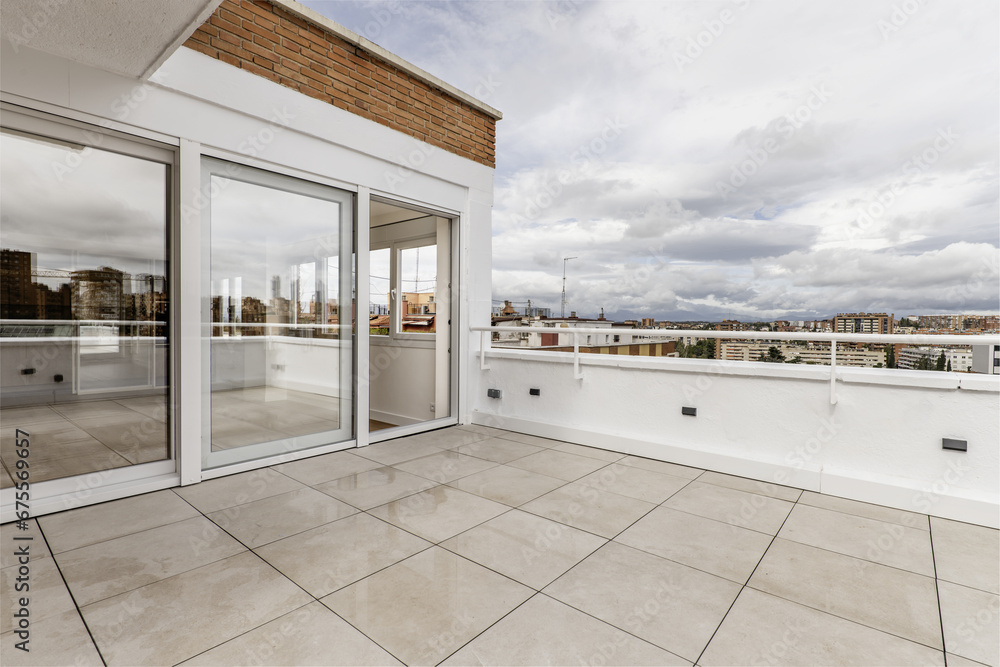 Terrace with white stoneware floor, large window with three aluminum and white glass doors, combined brick and white plaster walls, views of the city on a day full of clouds Terrace with white stoneware floor, large window with three aluminum and white glass doors, combined brick and white plaster walls, views of the city on a day full of clouds