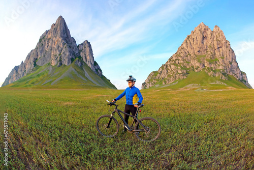 cyclist with a bicycle is resting on a green field against a blue sky. sports and recreation in nature