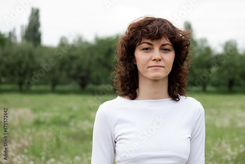 Mid shot attractive yoga instructor girl. Young sports woman in white sportswear on nature background. Calm female concentrated looking to camera. Concept of outdoors meditations coach