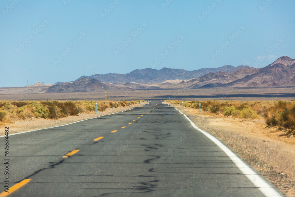 View of Mojave Desert national reserve landscape, an arid rain-shadow desert, California, United States of America, summer sunny day with road, mountains, sand dunes and a blue sky