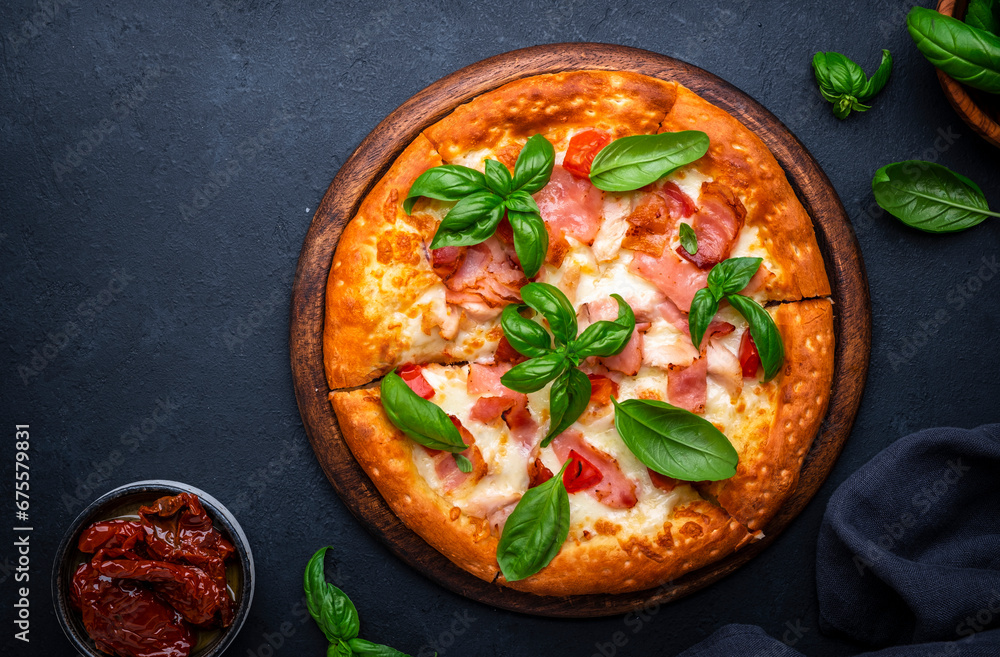 Homemade hot pizza with smoked ham, cheese, spicy tomato sauce and green basil on black table background, top view Homemade hot pizza with smoked ham, cheese, spicy tomato sauce and green basil on black table background, top view