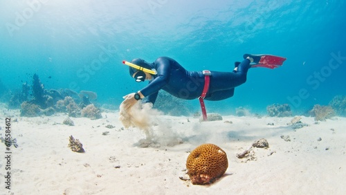 Male freediver glides in the tropical sea over the sandy bottom and plays with sand