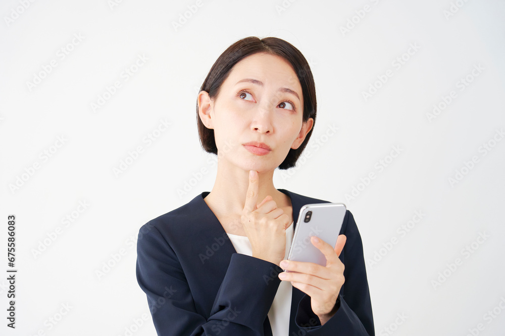 スマートフォンを持って考える中年のビジネスウーマン 白背景 スマートフォンを持って考える中年のビジネスウーマン 白背景
