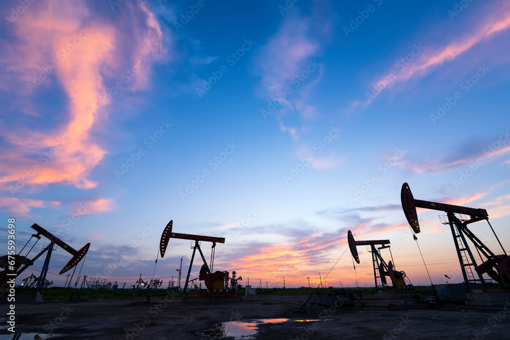 Fototapeta premium in the evening, oil pumps are running, The oil pump and the beautiful sunset reflected in the water, the silhouette of the beam pumping unit in the evening.
