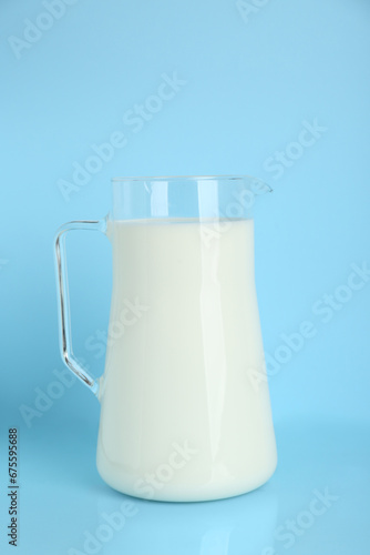 Jug of fresh milk on light blue background
