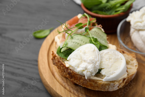 Tasty sandwich with burrata cheese, prosciutto and cucumber on grey wooden table, closeup