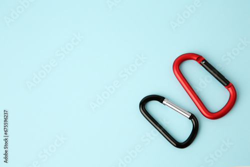 Two metal carabiners on light blue background, flat lay. Space for text