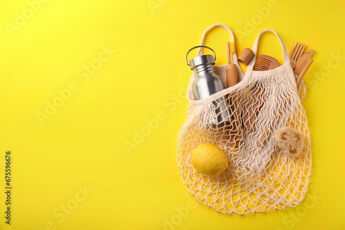 Fishnet bag with different items on yellow background, top view and space for text. Conscious consumption