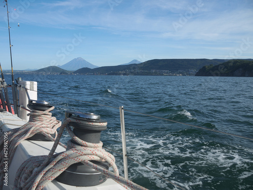 Yachting on Kamchatka, sail ship side with rigging on clew winches and mountains with Koryaksky and Avachinsky volcanoes on the coast photo