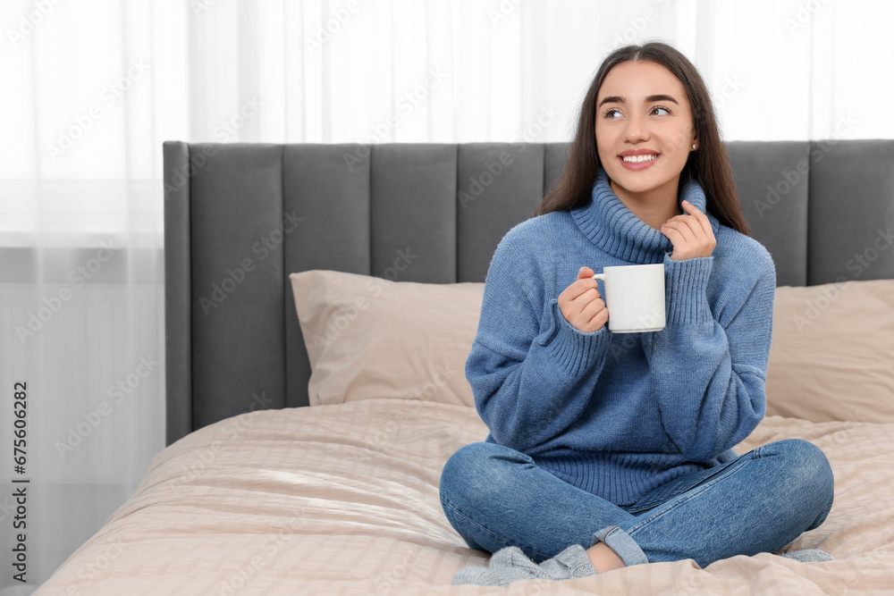 Happy young woman holding white ceramic mug on bed at home Happy young woman holding white ceramic mug on bed at home