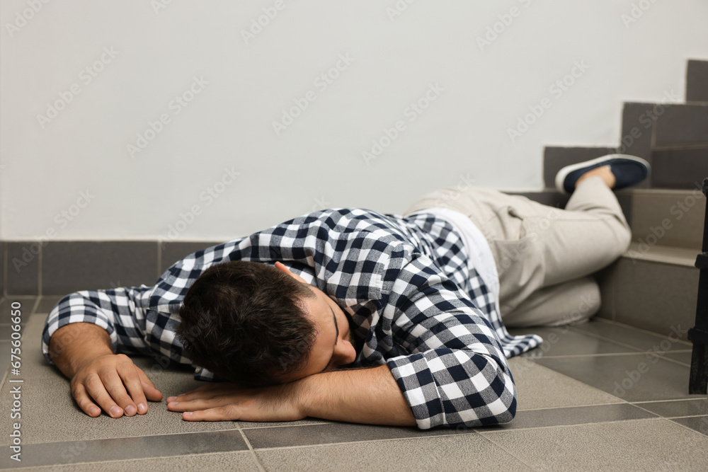 Unconscious man lying on floor after falling down stairs indoors Unconscious man lying on floor after falling down stairs indoors