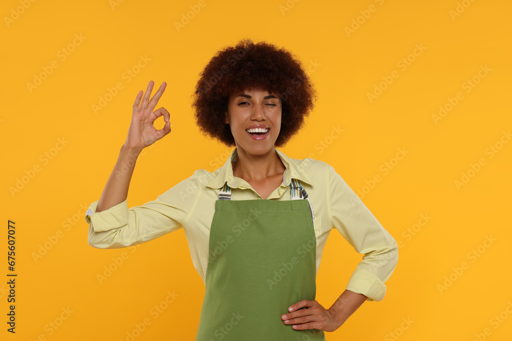 Happy young woman in apron showing ok gesture on orange background Happy young woman in apron showing ok gesture on orange background