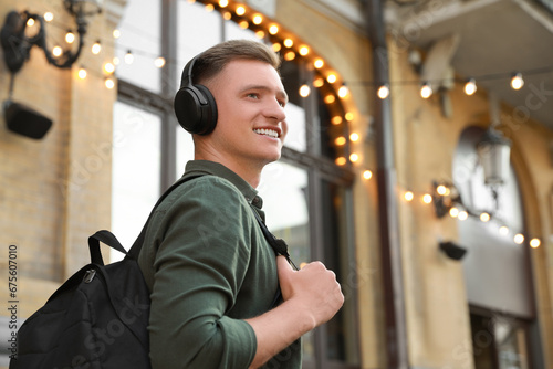 Smiling man in headphones listening to music outdoors. Space for text
