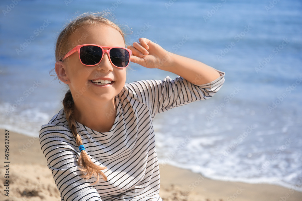 Happy little girl in stylish sunglasses on beach near sea Happy little girl in stylish sunglasses on beach near sea
