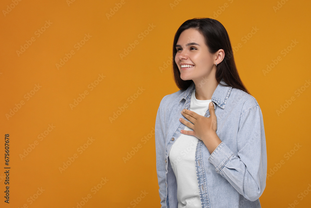 Thank you gesture. Happy grateful woman with hand on chest against orange background, space for text Thank you gesture. Happy grateful woman with hand on chest against orange background, space for text