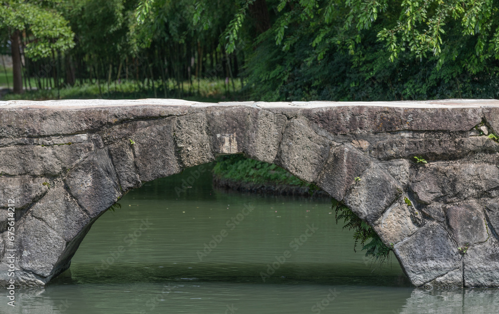 An arched stone bridge over a park pond.