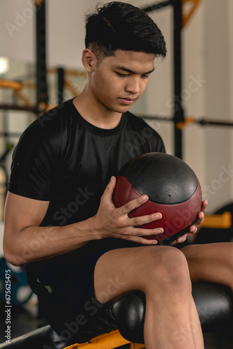 A young handsome asian man holding a medicine ball while sitting on the decline bench. Working out at the gym.