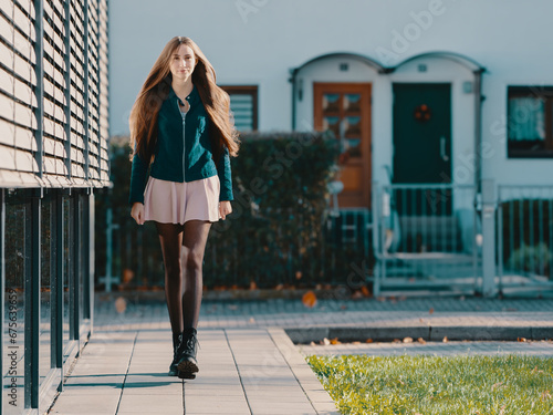 a young woman in a short skirt, black tights and long hair walks along glass display cases; ​ photo