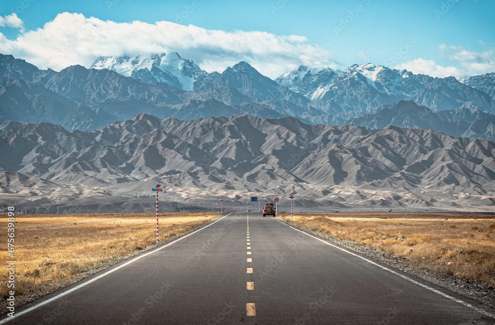 Fototapeta premium The view of a straight highway going towards the snow capped mountains in regional area in Xinjiang