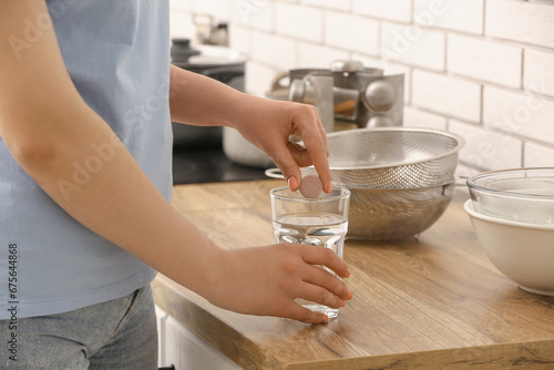 Woman putting effervescent tablet into glass of water on kitchen counter