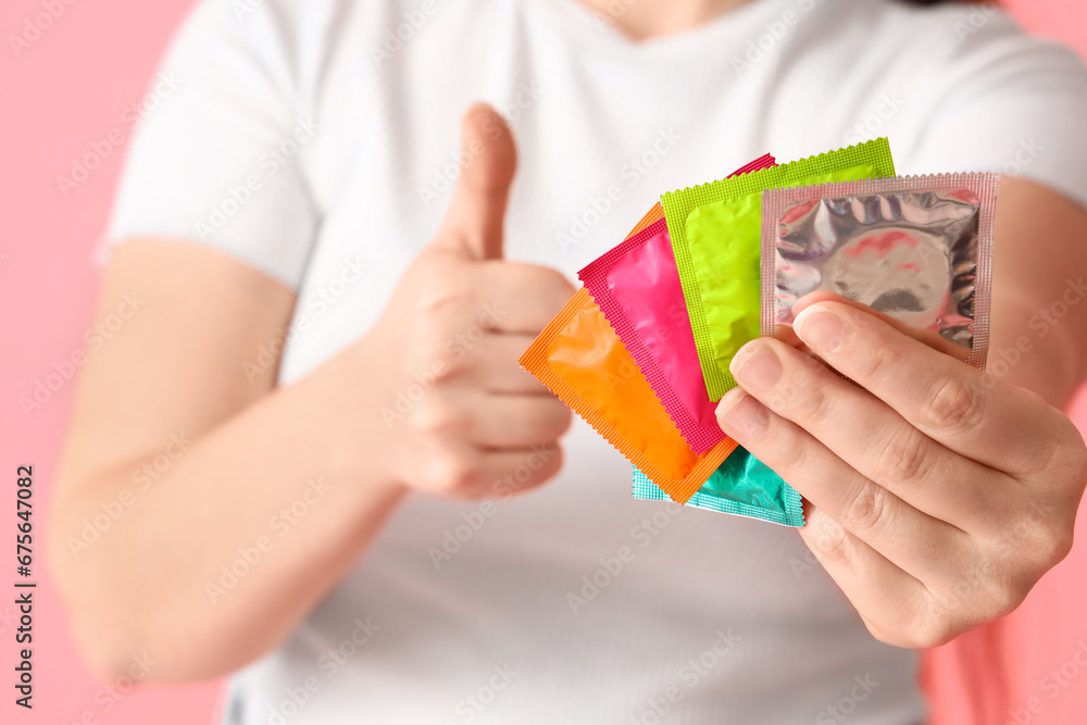 Young woman with condoms showing thumb-up on pink background, closeup Young woman with condoms showing thumb-up on pink background, closeup