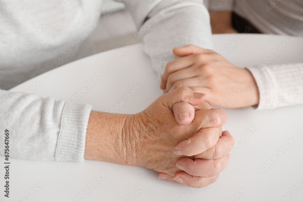 Young woman with her grandmother holding hands at table in kitchen, closeup Young woman with her grandmother holding hands at table in kitchen, closeup