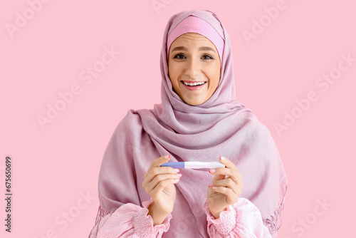 Fotomurale Happy beautiful young woman in hijab with pregnancy test on pink background