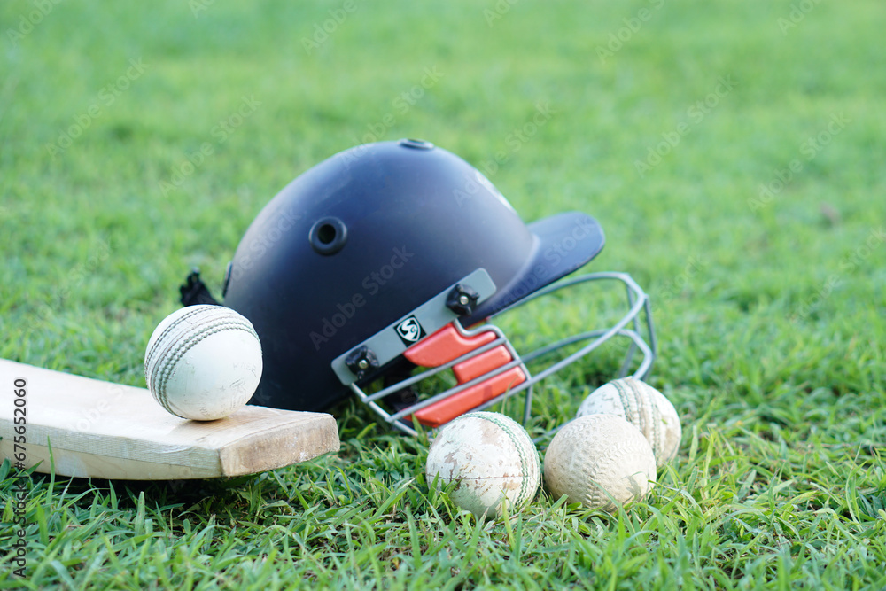 Cricket kits, helmet, cricket balls and bat on grass field. Concept