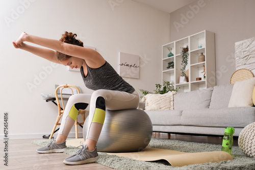 Beautiful young woman in sportswear exercising on fitness ball at home photo
